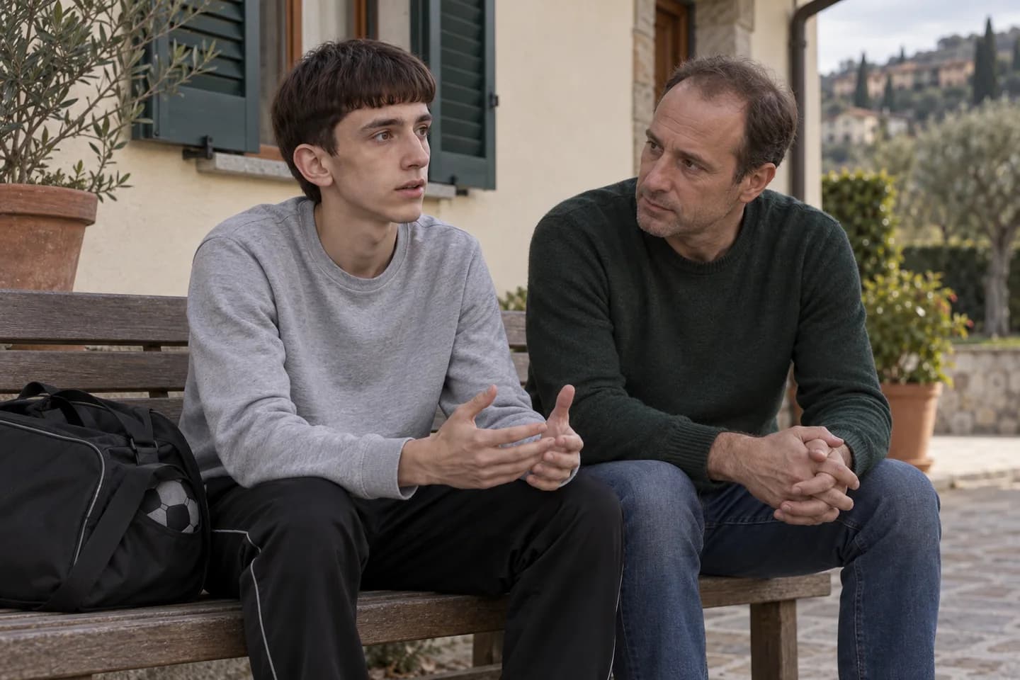Lo stesso ragazzo parla con il padre seduto su una panchina vicino a casa, con il borsone accanto. Scena illustrativa generata con AI.