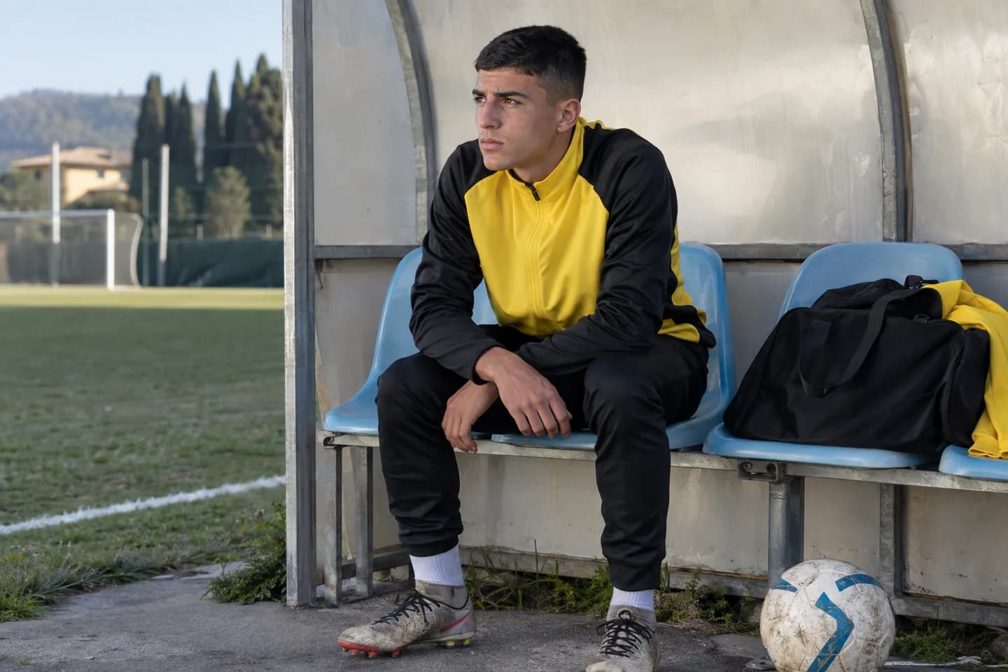 Un ragazzo in giacca gialla e nera segue il gioco dalla panchina dei sostituti. Scena illustrativa generata con AI.